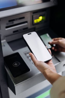 ATM 'de akıllı telefon kullanan, makineye kartı sokan, teknolojinin bankacılık ve dijital işlemlerin kolaylığını vurgulayan şahıs