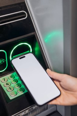 El ele tutuşan akıllı telefon, bankamatik ve finans hizmetlerinde teknolojinin entegrasyonunu vurgulayan aydınlatılmış tuş takımı ve ekran ile ATM yakınlarında konumlandırılmıştır.
