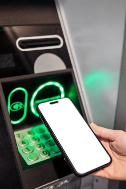 Parlak tuş takımlı bir ATM 'nin yanına yerleştirilen akıllı telefon modeli, teknolojinin bankacılığa entegrasyonunu ve dijital işlemlerin kolaylığını vurguluyor