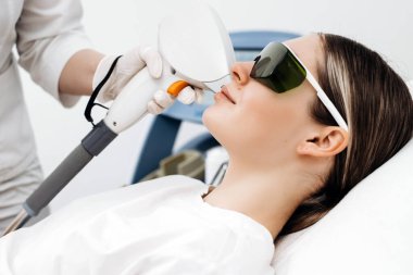 Kahverengi saçlı kadın klinik bir ortamda koruyucu gözlük takarken lazer tüyü temizleme tedavisi görüyor.