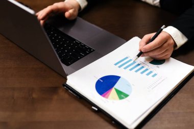 İşletme profesyoneli finansal verileri panoda haritalarla gözden geçirirken, bir dizüstü bilgisayar da notlar için tutulan ahşap bir masanın üzerine yerleştiriliyor.