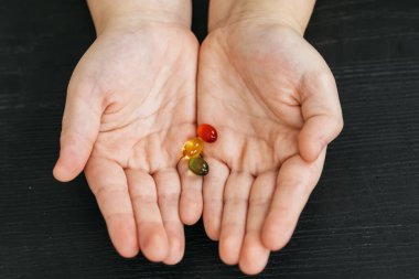 Çocuğun elleri, koyu ahşap arka planda kırmızı, sarı ve yeşil renkli üç şekerleme sergiliyor. Şekerlerin canlı renklerini ve dokularını gözler önüne seriyor.