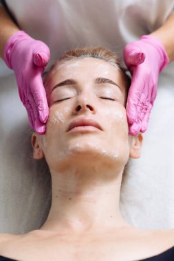 Güzellik salonunda güzellik uzmanıyla yüz maskesi takan genç bir kadın.