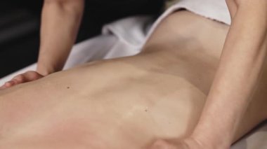 Karın üstü uzanan bir kadın masaj masasına sırt masajı yaptırıyor. Etrafı yumuşak ışıklandırma ve rahatlatıcı renklerle dolu sakin bir spa setiyle çevrili.