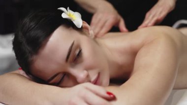 Karın üstü uzanan bir kadın masaj masasına sırt masajı yaptırıyor. Etrafı yumuşak ışıklandırma ve rahatlatıcı renklerle dolu sakin bir spa setiyle çevrili.