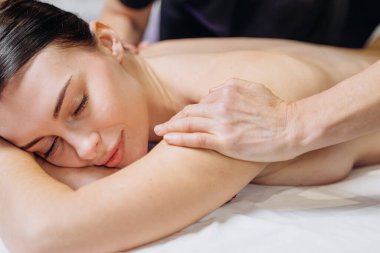 Kadın beyaz bir masada masaj yapmayı seviyor. Bir terapistin eli nazikçe sırtını kapalı bir ortamda tedavi ediyor.