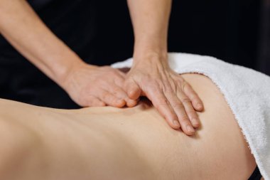 Masaj terapisti, bir müşterinin beline baskı uygulamak için elini kullanır. Tedavi masasında, sakinleştirici spa ortamında beyaz bir havluyla yatar.