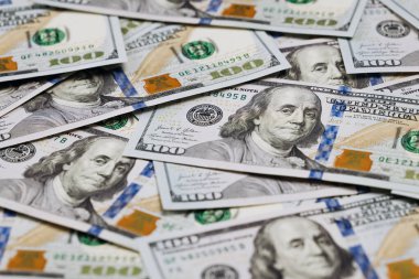 Birkaç yüz dolarlık banknotların yakın plan görüntüsü dağınık bir düzende serilmiş ve paranın detaylı tasarımı ve özellikleri vurgulanmış.