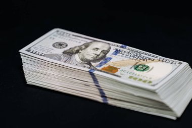 Karanlık bir arka planda düzgünce düzenlenmiş yüz dolarlık banknotlar banknotların karmaşık tasarım ve güvenlik özelliklerini vurguluyor.