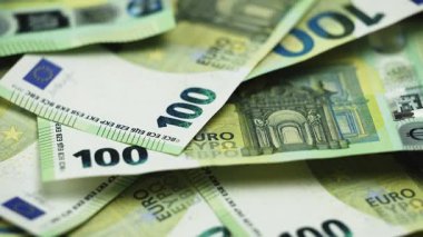 Bir yüzeyde 50 ve 100 banknotluk çeşitli avro banknotları sergilenirken, arka planda ek para birimi kısmen görülebilir