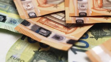 Bir yüzeyde 50 ve 100 banknotluk çeşitli avro banknotları sergilenirken, arka planda ek para birimi kısmen görülebilir