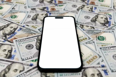 100 dolarlık banknotların geniş bir alana yerleştirilmiş boş ekranlı akıllı telefon, cihazın etrafındaki para birimi ile finansal temayı vurguluyor.
