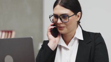 Yetişkin, beyaz, gözlüklü, akıllı telefonlu, dizüstü bilgisayar kullanan bir kadın.