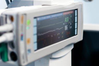 Tıbbi cihaz ekranında, sağlık teknolojisi ve hasta izleme sistemlerini vurgulayan klinik bir ortamda yaşam belirtileri ve dalga biçimleri görülüyor.