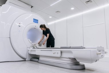 Kadın teknisyen MRI makinesini çağdaş bir tıbbi ortamda düzelterek, temizlik ve teknolojiye odaklanarak hasta muayenesine hazır hale getiriyor.