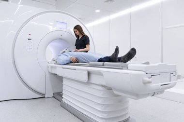 Hasta MRI makinesinde yatarken, teknisyenler gelişmiş görüntüleme teknolojisi ve steril bir çevreye sahip modern bir tıbbi tesiste taramaya hazırlanıyor.