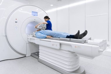 Teknisyen ekipmanları parlak ışıklandırma ve steril çevreye sahip çağdaş bir tıbbi ortamda ayarlarken hasta MRI masasında konumlandırıldı.