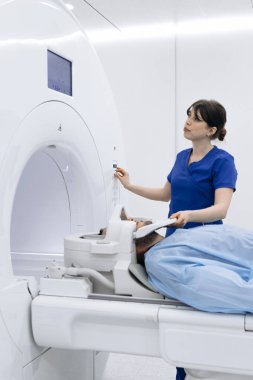 Hasta MRI makinesinde yatarken teknisyen ayarları ayarlar ve süreci modern, iyi aydınlatılmış bir tıbbi muayene odasında izler.
