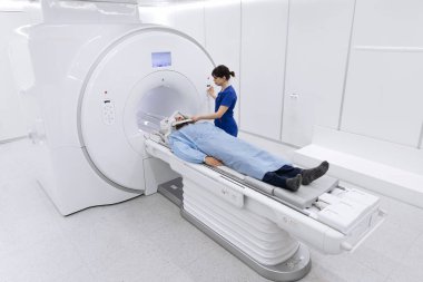 MRI makinesine yerleştirilmiş hasta, teknisyen olarak parlak ve steril bir çevreye sahip modern bir tıbbi tesiste görüntülemeye hazırlanıyor.