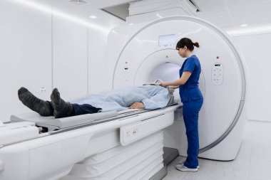 Hasta MRI makinesinde yalan söylerken, sağlık uzmanları temiz ve beyaz çevreye sahip modern bir tıbbi tesiste taramaya hazırlanıyor.