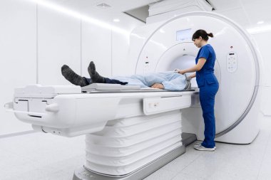 MR makinesine yerleştirilmiş hasta mavi önlüklü teknisyen olarak gelişmiş görüntüleme teknolojisiyle modern ve parlak bir tıbbi tesiste ayarlar yapıyor.