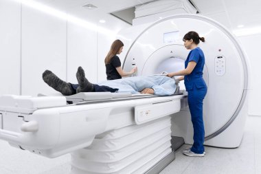 Hasta MRI makinesine yerleştirilirken, önlüklü tıp uzmanları çağdaş bir tıbbi ortamda görüntüleme işlemine hazırlanıyorlar.