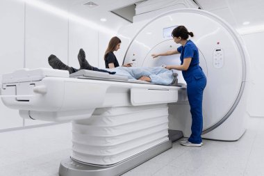 Hasta MRI makinesinde yalan söylerken, sağlık uzmanları da parlak ve steril çevresi olan modern bir tıbbi tesiste tarama için hazırlanıyor.