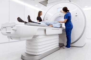 MRI masasına yerleştirilmiş hasta sağlık uzmanları gelişmiş teknolojili, parlak ve modern bir tıbbi tesiste taramaya hazırlanıyor.