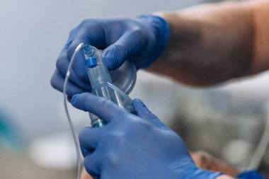 Mavi eldivenli bir tıp çalışanı, arka planda bulanık elementlerin bulunduğu klinik bir ortamda endotrakeal entübasyon aletleri birleştirir.