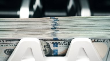 Para sayma makinesi 100 dolarlık banknotları ve makinenin iç bileşenlerini yakın perspektifte görüntüler.