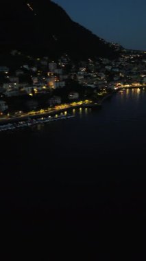 Como Gölü 'nün mehtap ve şehir ışıklarıyla çekilmiş sinematik insansız hava aracı görüntüleri sosyal medya için dikey formatta ayna benzeri suya yansıyor.