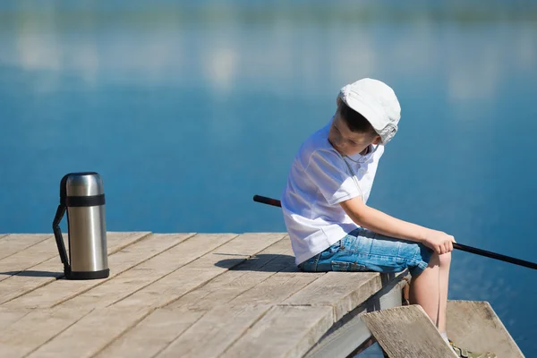 桟橋での釣りの魔法瓶に紅茶を探して少年 — ストック写真
