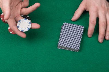 Yeşil masada bir deste kağıt var ve krupiyenin elleri bir fiş tutuyor, poker oynuyorlar.