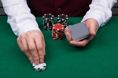 Satıcının elleri bir deste kağıt tutuyor ve poker masasına çip koyuyor.