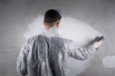 Koruyucu üniformalı bir işçi son macunu beton duvara, dikiz aynasına uygular.