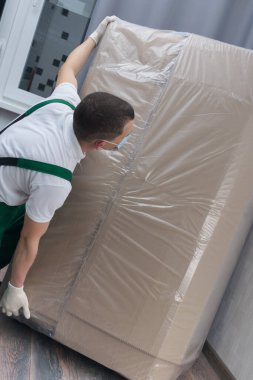 Koruyucu maske ve eldiven takan yükleyici, müşterinin evine büyük bir kutu teslim eder.