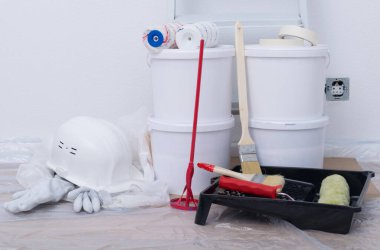 Bir set fırça, bir mikser ve dört kova boya, beyaz bir duvara karşı yakın çekim