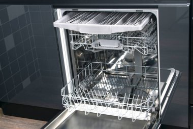 view of the inside of the dishwasher with empty nets for kitchen utensils, against the background of a dark kitchen clipart