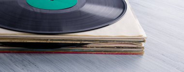 Gri bir masada, arka planda kağıt kutularda bir yığın vinil kayıt var.