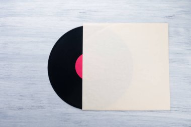 Açık gri arka planda kağıt bir zarfın içindeki vinil bir kayıt var.