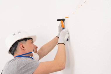 Miğferli bir işçi çekiçle beton bir duvara vuruyor.