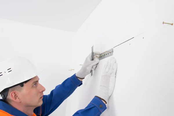 a worker on a white wall, sets a bar for fixing kitchen furniture cabinets