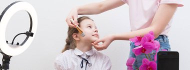 Mola sırasında, yüzük lambasının ışığı altında, blogcu kız, masada, görüntülü sohbet için hazırlanıyor, asistan makyaj yapıyor, yakın plan.