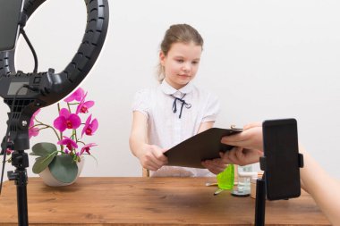 Mola sırasında, yüzük lambasının ışığı altında, blogcu kız, masada, video sohbeti için hazırlanıyor, asistan senaryoyu gösteriyor.