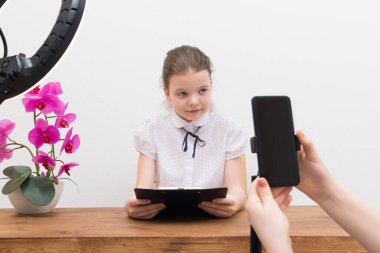 Mola sırasında, yüzük lambasının ışığı altında, masadaki blogcu kız görüntülü bir sohbet için hazırlanıyor, asistan senaryoyu gösteriyor ve telefonu açıyor.