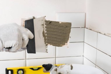 Bir malayla el, duvar yüzeyine fayans yapıştırıcısı sürer.