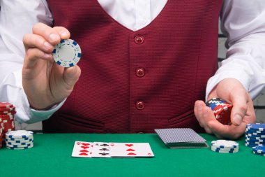 Krupiyenin elinin kırmızı yelek ve yeşil poker masasının arka planında çipin üzerindeki yazıtlar için bir yer var.
