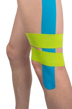 Beyaz arka planda, Kinesio bantlı bir adamın bacağı, rahat spor ve sakatlıklardan korunmak için yapıştırılmış.