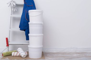 on the background of a white wall with a place for writing, building materials, buckets of paint, rollers, a stepladder and protective clothing