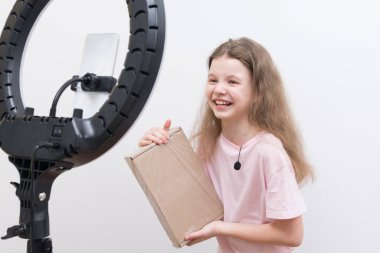 Neşeli bir kız blogcu, dairesel bir ışık ve akıllı bir telefon önünde, paketleri açmak için bir gözden geçirme yapar.